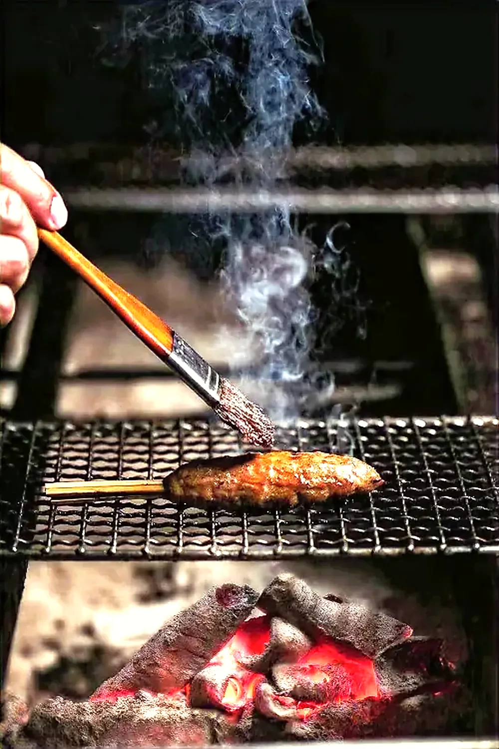 A skewer basted with tare over glowing charcoal