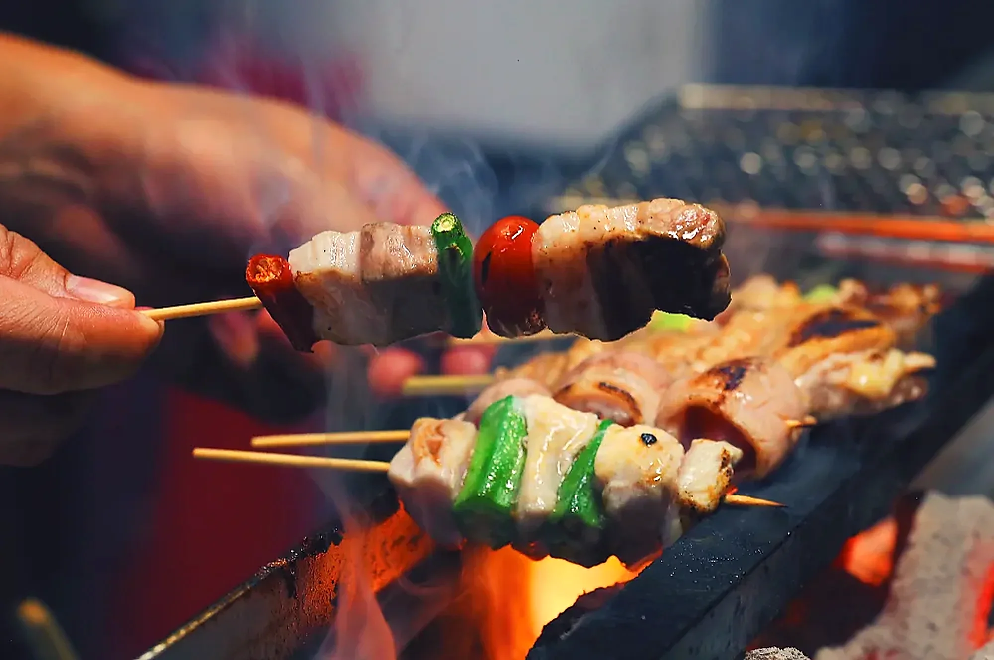 A chef turning skewers of pork and capsicum over open flame