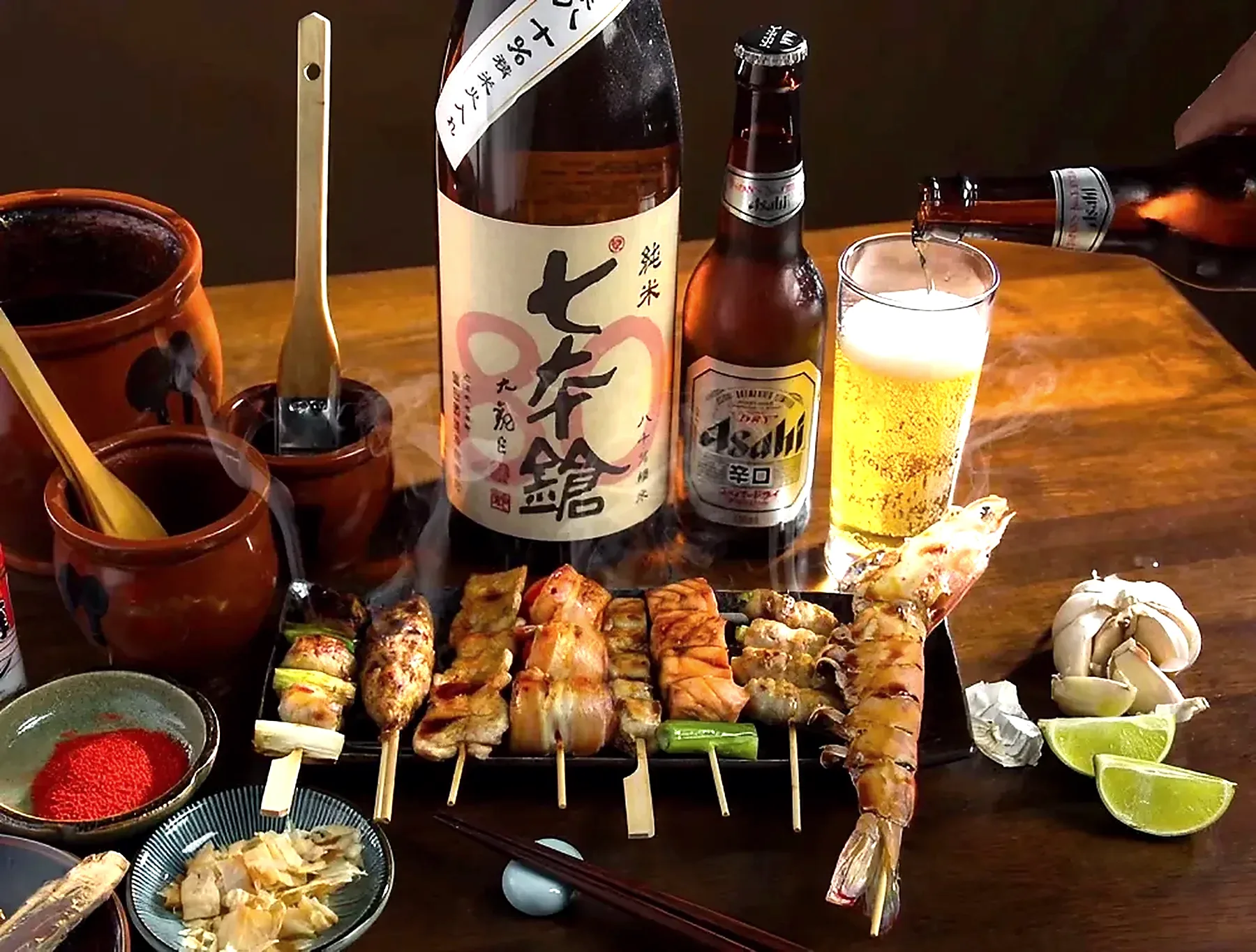 Skewers, sake and a beer on a timber table, shot from above
